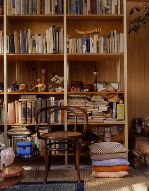 Interior view of the Eames House showing a bookshelf full of books, a wooden desk chair, and other assorted vintage objects
