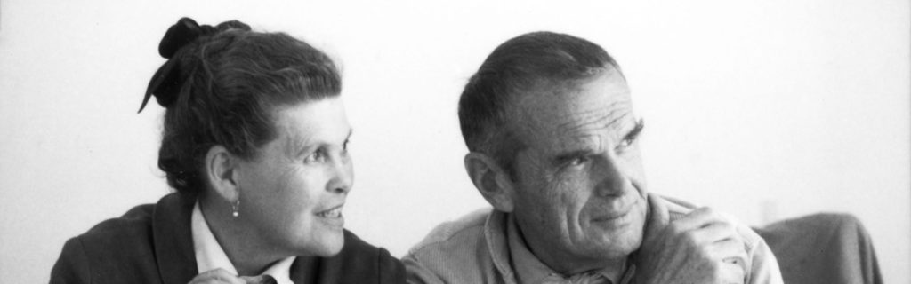 Ray and Charles Eames are seated in an office looking off camera out a window